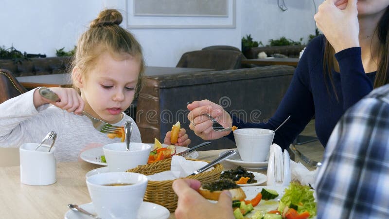 La famille prennent le déjeuner sain au restaurant Petite fille mangeant de la salade végétale avec du pain blanc photographie stock La famille prennent le déjeuner sain au restaurant Petite fille mangeant de la salade végétale avec du pain blanc photographie stock