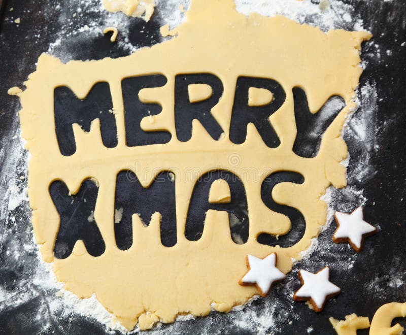 Text Merry Christmas cut out in rolled dough on a floury surface with star biscuits for fun Christmas baking. Text Merry Christmas cut out in rolled dough on a floury surface with star biscuits for fun Christmas baking