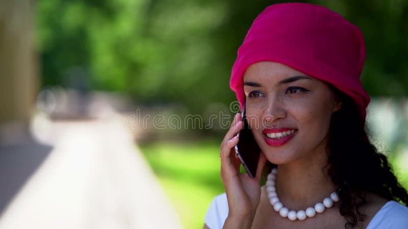 La femme adorable de mulâtre appelée par le téléphone portable debout dans le sourire de charme du parc banque de vidéos