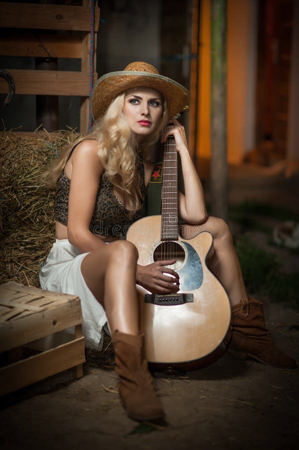 La femme attirante avec le regard de pays, a à l'intérieur tiré, style campagnard américain Fille blonde avec le chapeau et la gu image libre de droits La femme attirante avec le regard de pays, a à l'intérieur tiré, style campagnard américain Fille blonde avec le chapeau et la gu image libre de droits