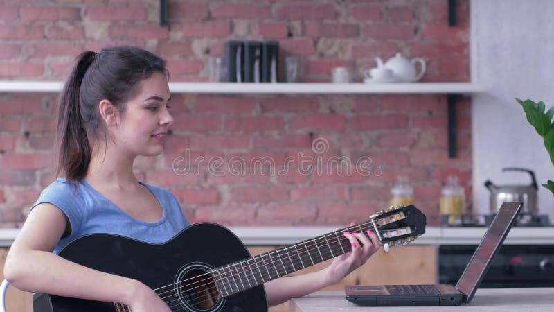 La femme attirante de guitariste apprenant l'instrument de musique ficelÃ© par jeu utilise l'ordinateur portable avec l'enseignem