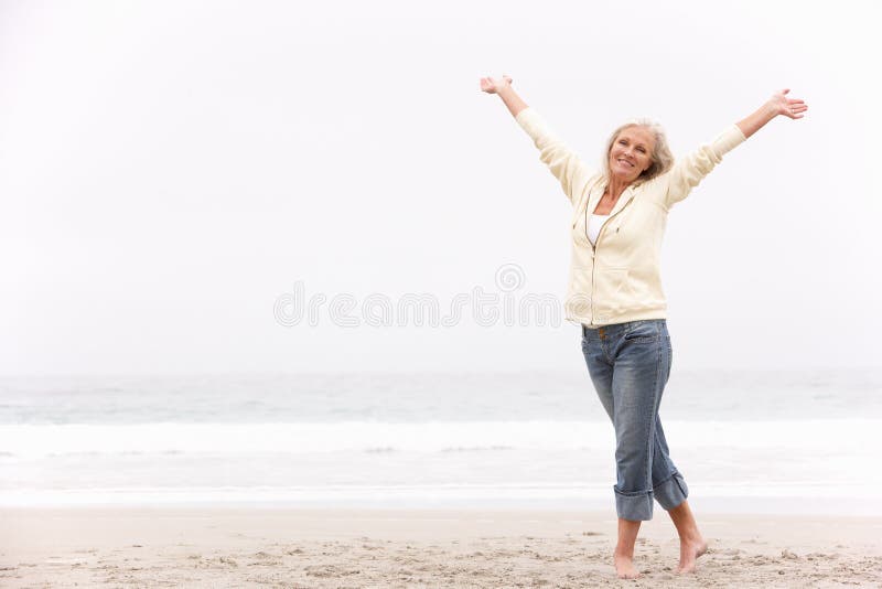 La femme aînée avec des bras a tendu sur la plage photographie stock La femme aînée avec des bras a tendu sur la plage photographie stock