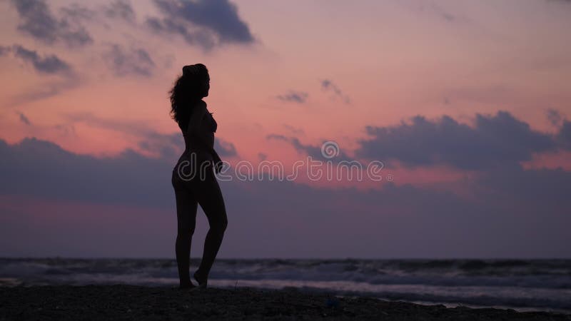 La femme dans des maillots de bain apprécient le coucher du soleil à la plage de mer