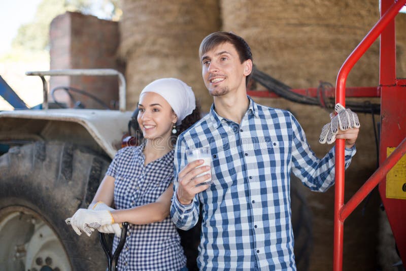 La femme de pays donnent au verre de conducteur de tracteur de l'homme de lait ? la ferme photographie stock La femme de pays donnent au verre de conducteur de tracteur de l'homme de lait ? la ferme photographie stock