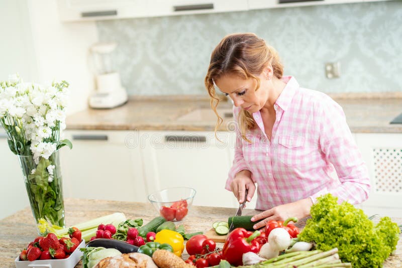 La femme de sourire coupe en tranches le concombre sur une table de cuisine photographie stock libre de droits La femme de sourire coupe en tranches le concombre sur une table de cuisine photographie stock libre de droits