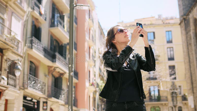 La femme de touristes attirante faisant un selfie emploie un smartfone tout en marchant à la rue image libre de droits La femme de touristes attirante faisant un selfie emploie un smartfone tout en marchant à la rue image libre de droits