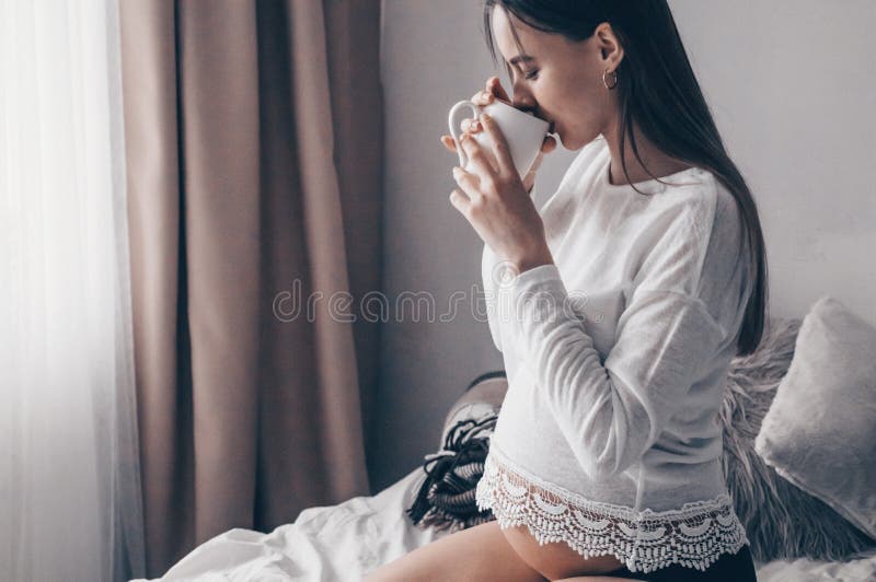 La femme enceinte attirante boit du thé sur le lit Thé potable regardant par une fenêtre à la maison Derniers mois de grossesse photo libre de droits La femme enceinte attirante boit du thé sur le lit Thé potable regardant par une fenêtre à la maison Derniers mois de grossesse photo libre de droits