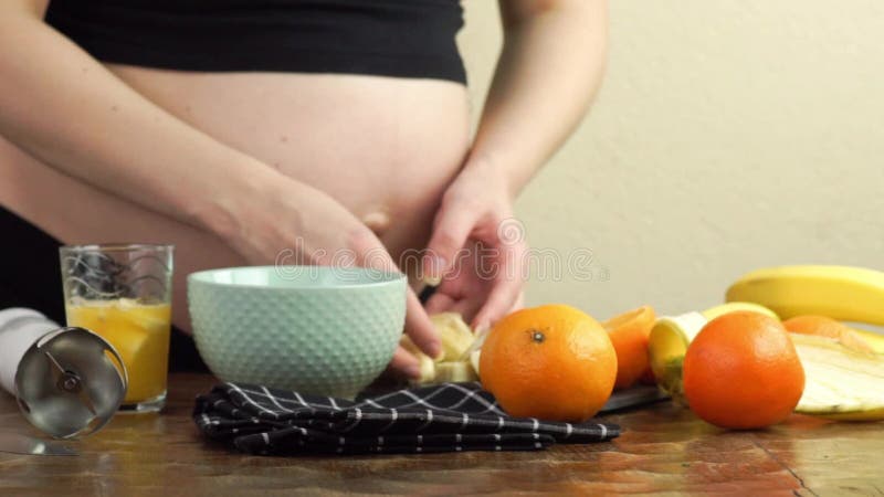 La femme enceinte fait une collation sain dans ses tranches de cuisine viennent des bananes et des oranges clips vidéos