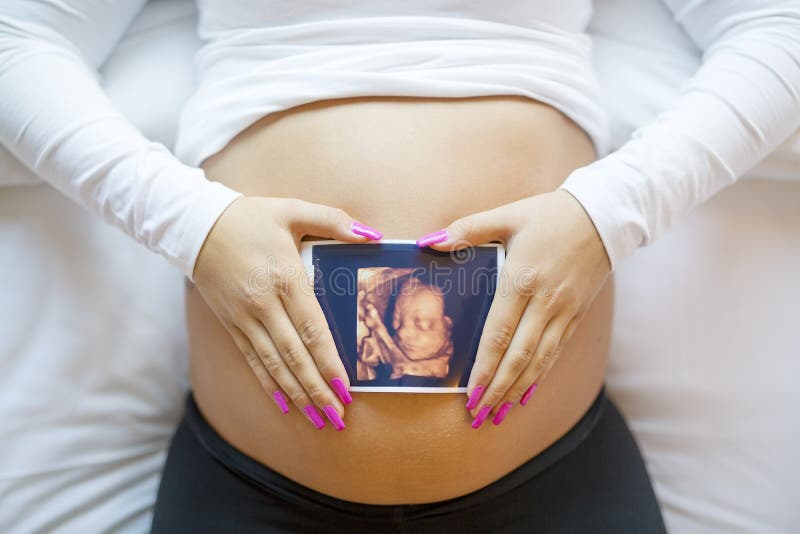 La femme enceinte tient la photo d'ultrason sur le ventre dans le lit photos libres de droits La femme enceinte tient la photo d'ultrason sur le ventre dans le lit photos libres de droits