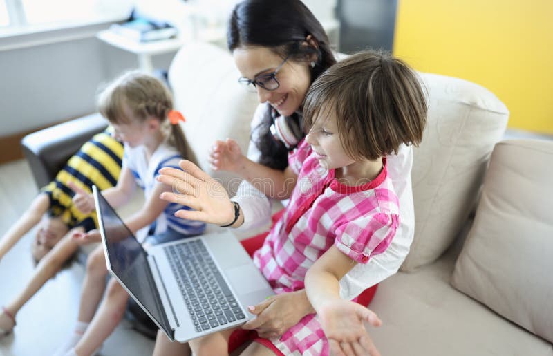 La femme est assise sur le canapé la fille est assise sur ses genoux ils regardent l'ordinateur portable à côté des enfants jouent photo stock