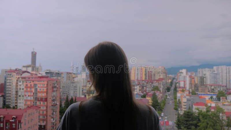 La femme est debout sur le balcon et regarde la ville dans l'après-midi banque de vidéos