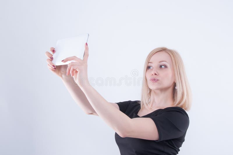 La femme faisant le selfie avec le comprimé sur le blanc a isolé le fond Fermez-vous de la jeune belle fille blonde dans la robe photographie stock libre de droits La femme faisant le selfie avec le comprimé sur le blanc a isolé le fond Fermez-vous de la jeune belle fille blonde dans la robe photographie stock libre de droits