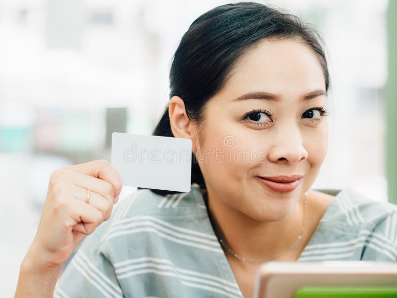 La femme heureuse emploie une carte de crédit blanche de maquette pour des achats en ligne sur le comprimé photographie stock La femme heureuse emploie une carte de crédit blanche de maquette pour des achats en ligne sur le comprimé photographie stock