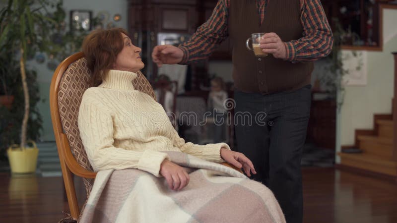 La femme mûre s'asseyant dans une chaise de basculage et son vieux mari lui a apporté une tasse de café et a doucement pressé sa