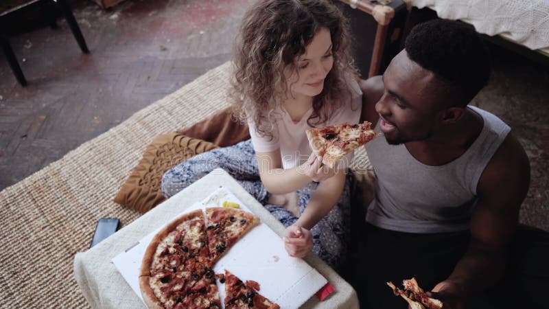 La femme offre la pizza pour équiper, mais pour manger la tranche seule Couples multiraciaux ayant l'amusement pendant le repas a photographie stock libre de droits La femme offre la pizza pour équiper, mais pour manger la tranche seule Couples multiraciaux ayant l'amusement pendant le repas a photographie stock libre de droits