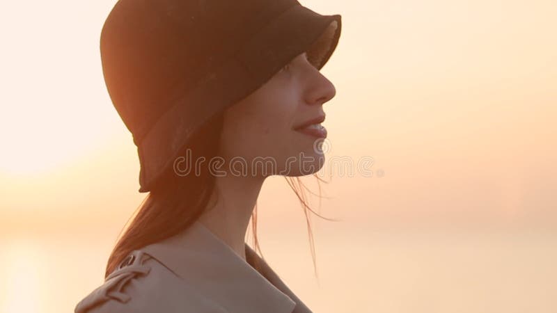 La femme pose pour la caméra et on dirait qu'avec le sourire tout en se tenant sur la plage de mer le soir d'automne. clips vidéos