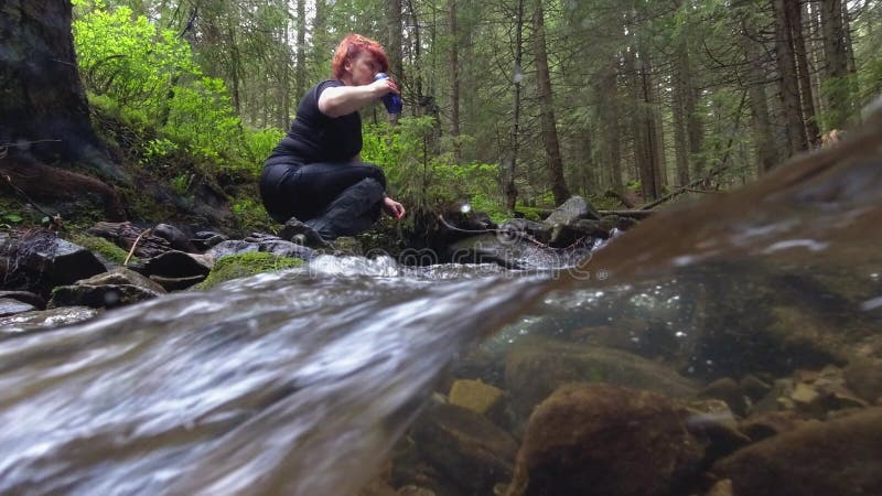 La femme prend de l'eau dans une tasse d'un ruisseau banque de vidéos