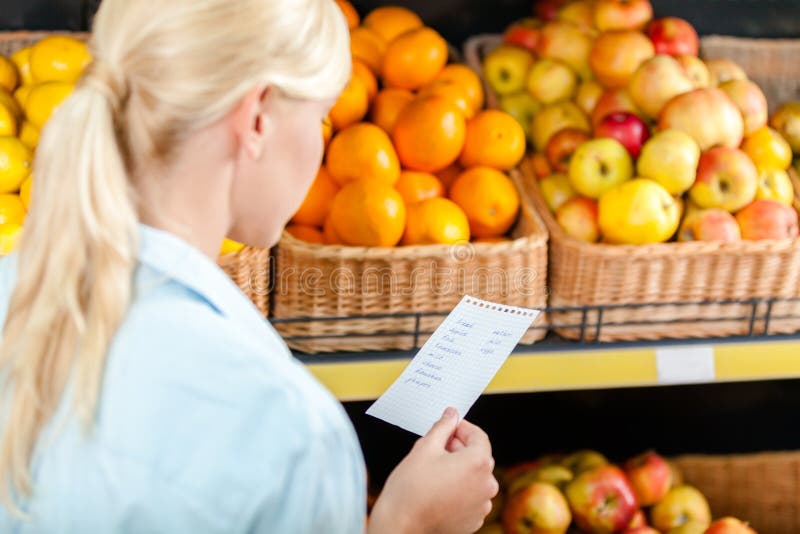 La femme regarde par la liste d'achats près de la pile des fruits
