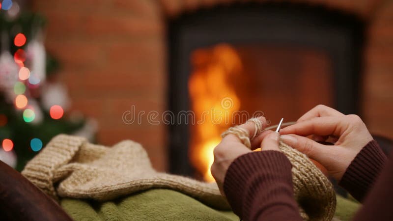 La femme remet les chaussettes de laine de tricotage au temps de Noël se reposant par le feu banque de vidéos