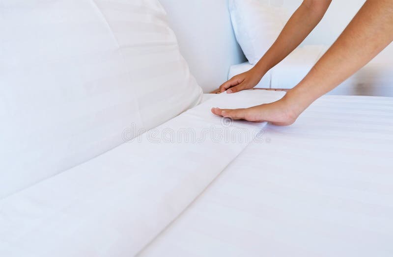 La femme remet à installation le drap blanc dans la chambre d'hôtel photographie stock libre de droits La femme remet à installation le drap blanc dans la chambre d'hôtel photographie stock libre de droits
