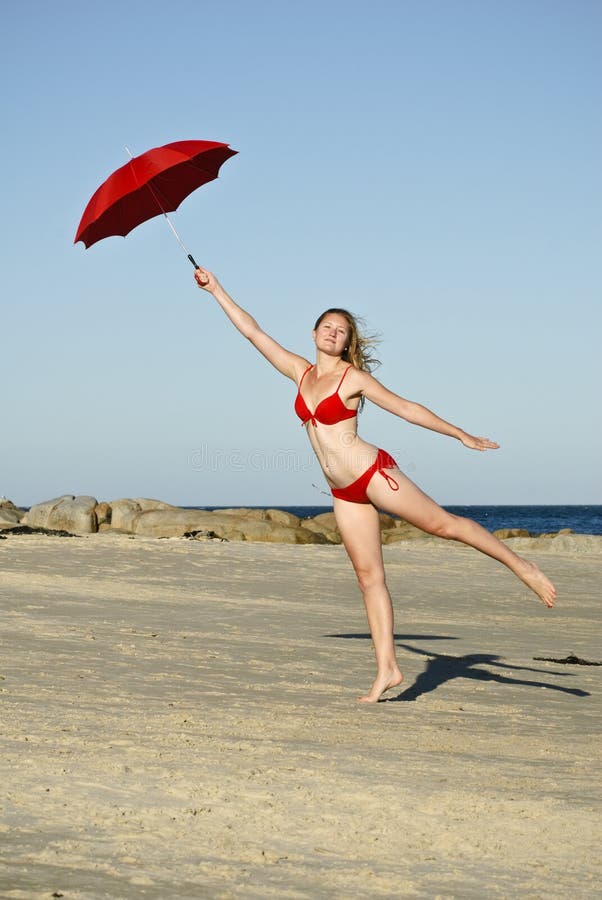 La femme sautant sur la plage avec le parapluie rouge photo stock La femme sautant sur la plage avec le parapluie rouge photo stock