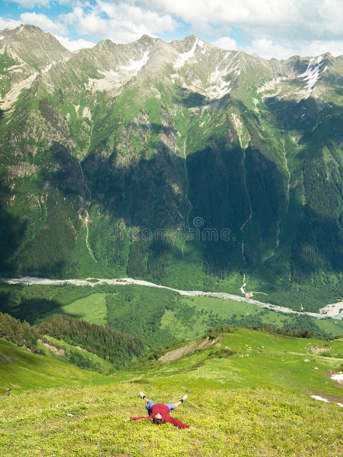 La femme se trouve sur des mains de champ de floraison tendues contre le contexte des montagnes majestueuses photographie stock libre de droits La femme se trouve sur des mains de champ de floraison tendues contre le contexte des montagnes majestueuses photographie stock libre de droits