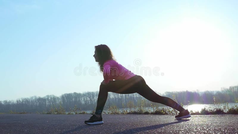 La femme sportive va chercher dedans des sports sur la berge au lever de soleil Mouvement lent