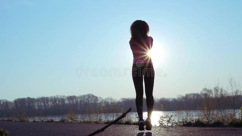 La femme sportive va chercher dedans des sports sur la berge au lever de soleil Mouvement lent