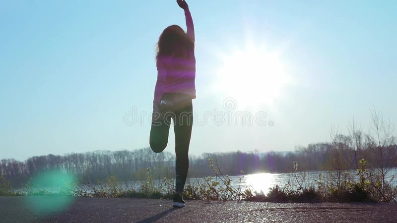 La femme sportive va chercher dedans des sports sur la berge au lever de soleil Mouvement lent