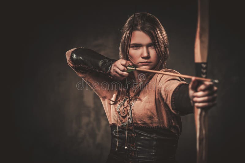 La femme sérieuse de Viking avec le tir à l'arc dans un guerrier traditionnel vêtx, posant sur un fond foncé photos libres de droits La femme sérieuse de Viking avec le tir à l'arc dans un guerrier traditionnel vêtx, posant sur un fond foncé photos libres de droits