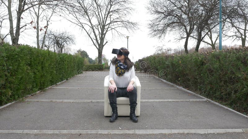 La femme utilise l'équipement de VR tout en détendant dans un fauteuil en parc banque de vidéos