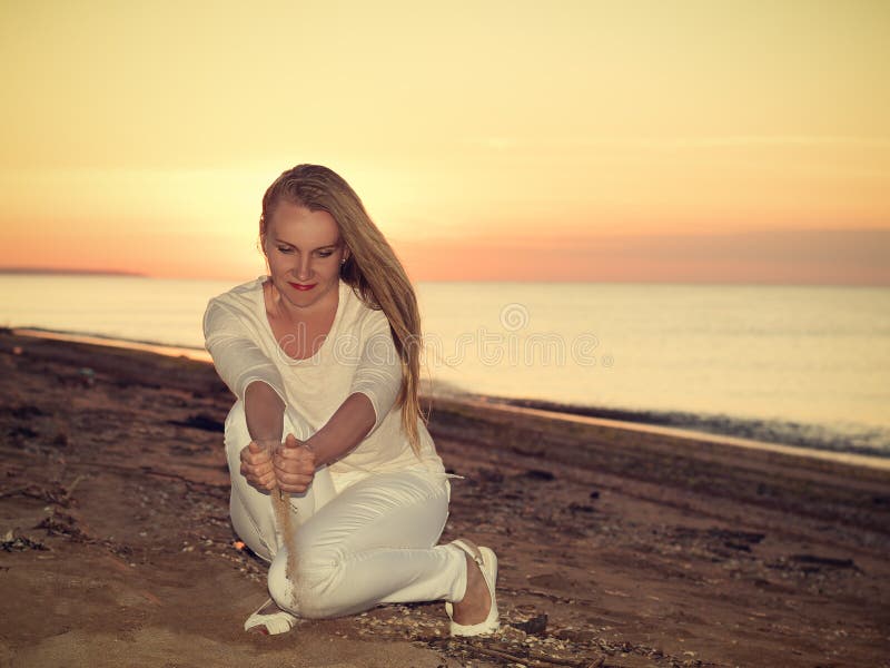 La femme verse des mains de sable au coucher du soleil sur la mer photo libre de droits La femme verse des mains de sable au coucher du soleil sur la mer photo libre de droits