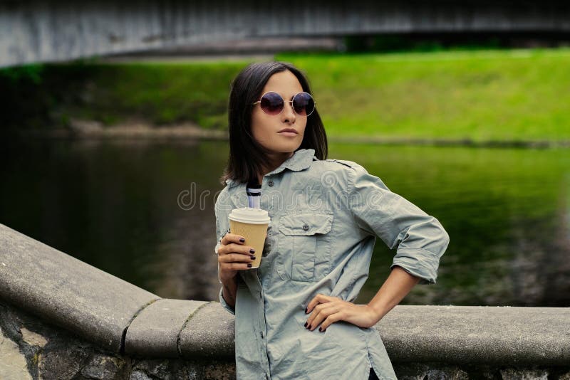 La femmina beve il caffè in movimento in un parco dell'estate vicino al lago
