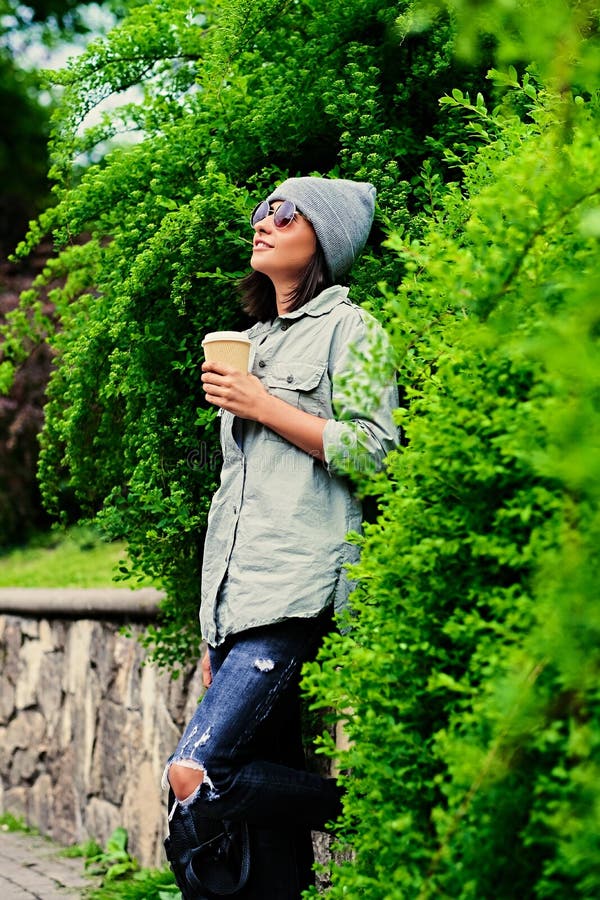 La femmina in occhiali da sole tiene la tazza di caffè di carta in un parco dell'estate