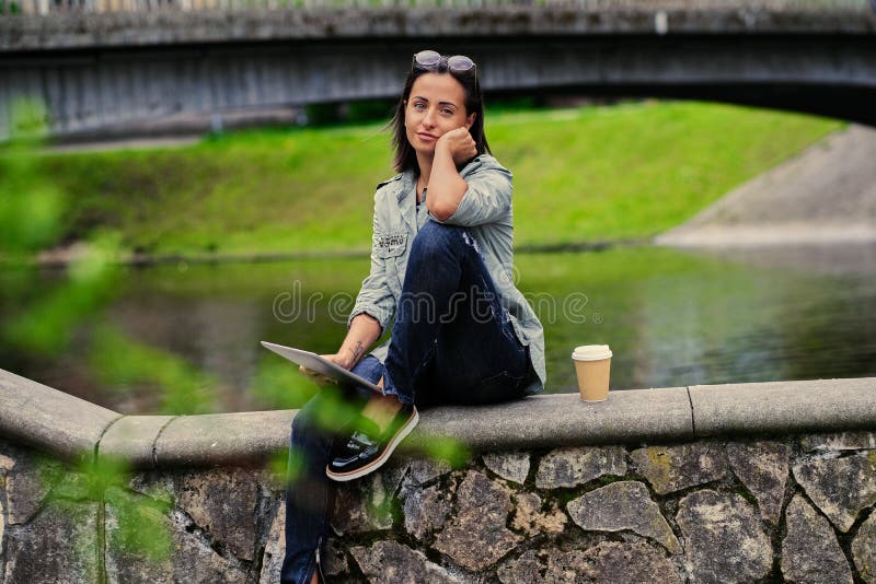 La femmina si siede su un ponte e tiene il PC della compressa