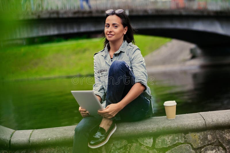 La femmina si siede su un ponte e tiene il PC della compressa