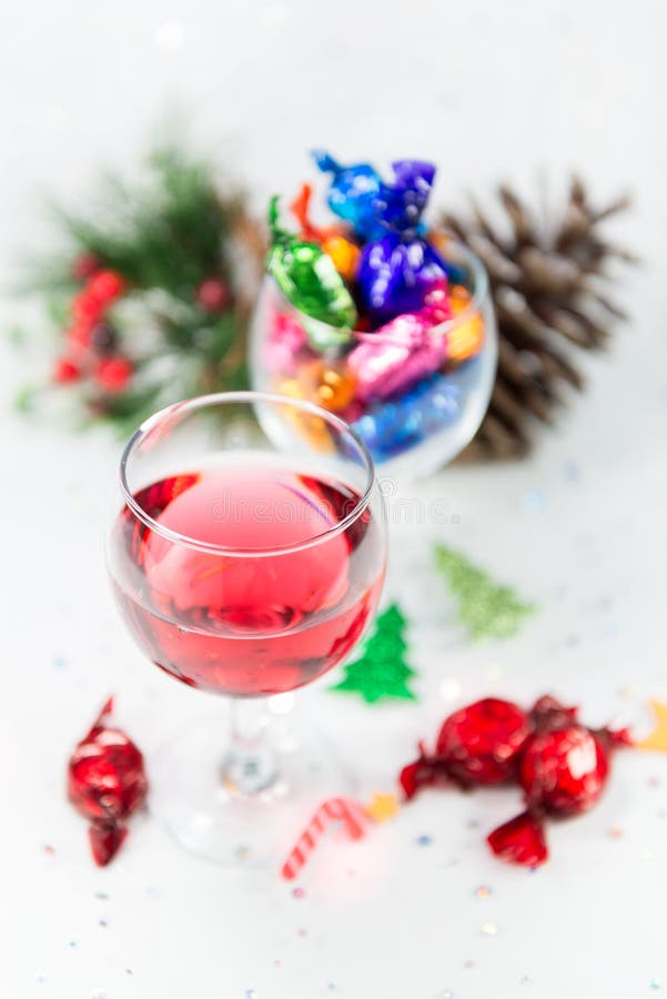 Christmas party celebrations with wine and wrapped chocolate candy sweets. Treats to enjoy the merry holiday season. On a snowy white background. Selective focus on wine glass. Christmas party celebrations with wine and wrapped chocolate candy sweets. Treats to enjoy the merry holiday season. On a snowy white background. Selective focus on wine glass.