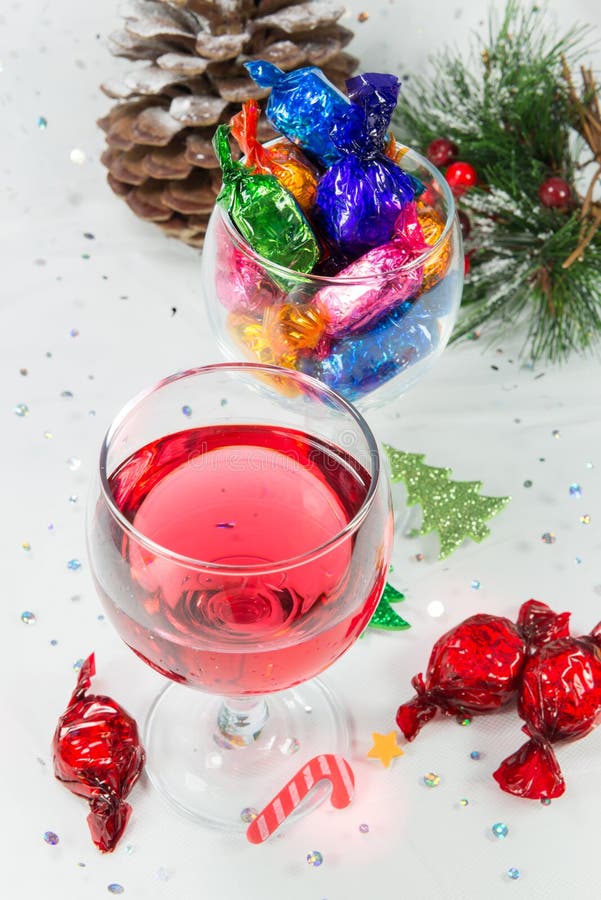 Christmas party celebrations with wine and wrapped chocolate candy sweets. Looking down on the treats for the happy holiday season. On a snowy white background. Christmas party celebrations with wine and wrapped chocolate candy sweets. Looking down on the treats for the happy holiday season. On a snowy white background.