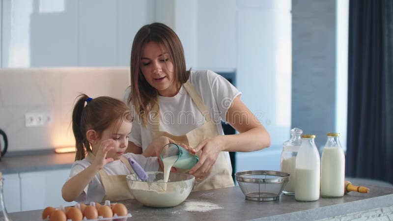 La figlia e la madre cucinano insieme. la donna versa il latte in impasto per inginocchiarsi.. la mamma è un'assistente