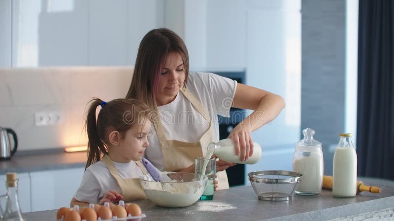 La figlia e la madre cucinano insieme. la donna versa il latte in impasto per inginocchiarsi.. la mamma è un'assistente