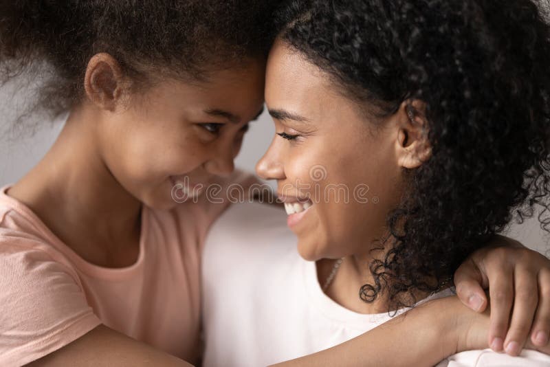 La figlia felice abbraccia la giovane madre chiusa faccia a faccia con un ritratto di famiglia