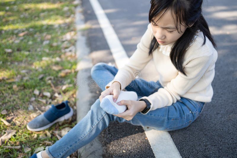 Asian child girl sitting on the floor and takes off a sneakers,hold her sore spot,sad female teenage rubbing and massaging her painful foot,fatigue,achy and tired from walk,run or stand for a long day. Asian child girl sitting on the floor and takes off a sneakers,hold her sore spot,sad female teenage rubbing and massaging her painful foot,fatigue,achy and tired from walk,run or stand for a long day