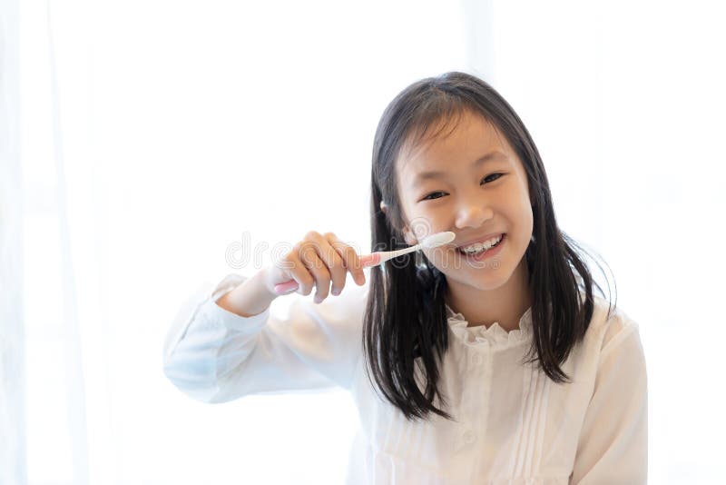 La fille asiatique sourit et tient une brosse à dents sur le fond blanc, concep sain de dents photos libres de droits