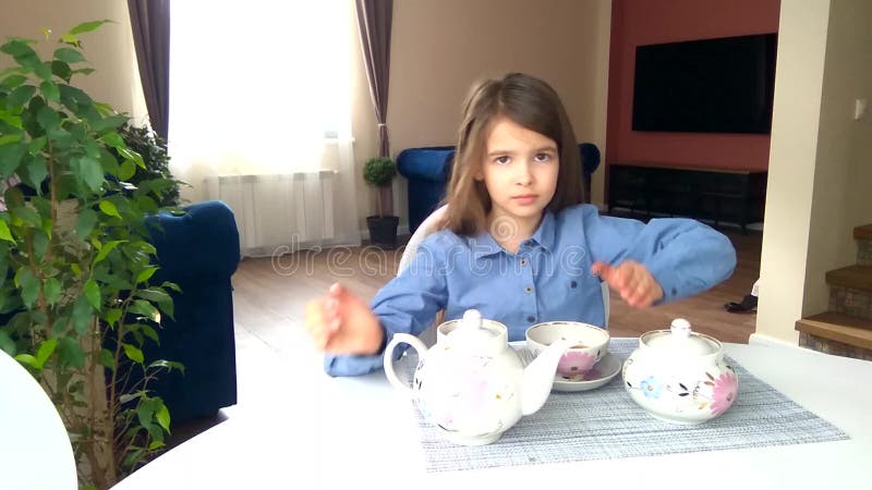 La fille assise à la table verse et boit du thé d'un gobelet