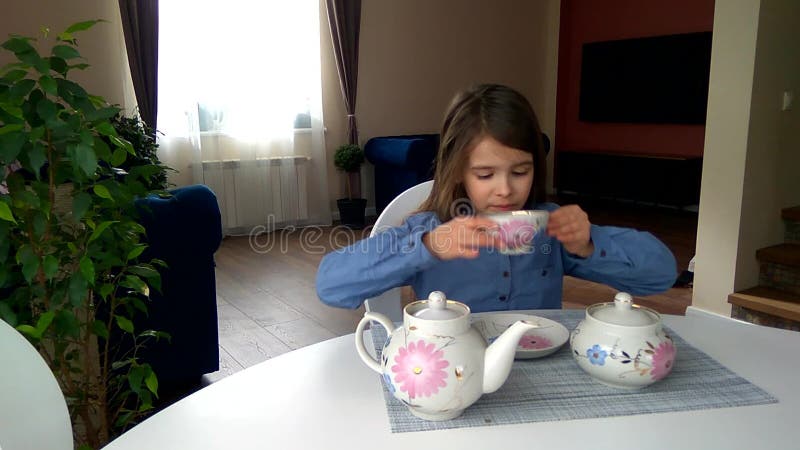 La fille assise à la table verse et boit du thé d'un gobelet