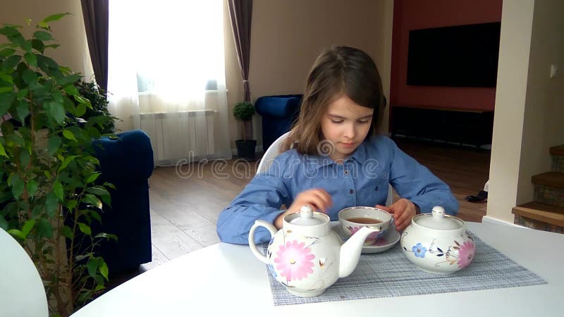 La fille assise à la table verse et boit du thé d'un gobelet