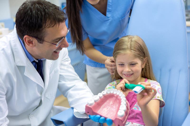 La fille avec la grande brosse à dents apprennent du dentiste comment brosser des dents image stock La fille avec la grande brosse à dents apprennent du dentiste comment brosser des dents image stock