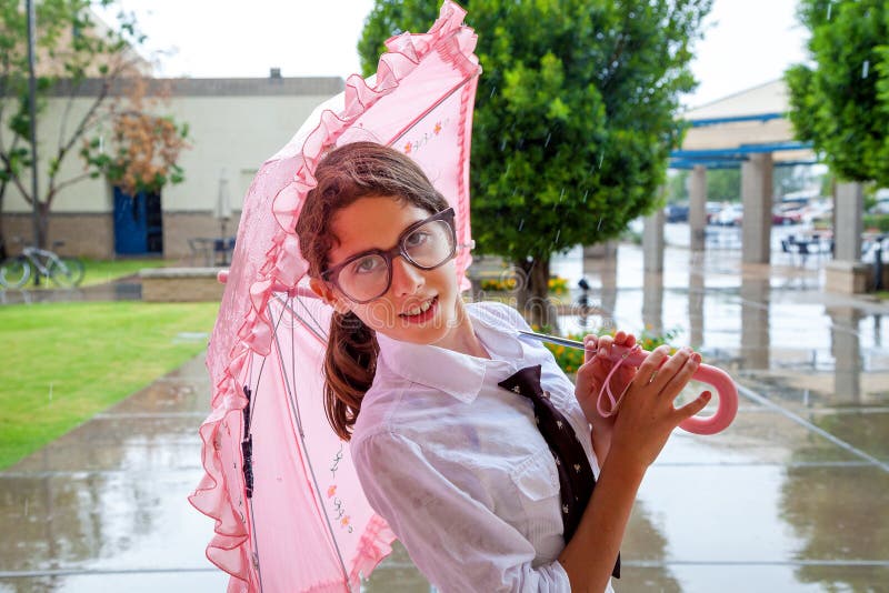 La fille avec le lien et les grands verres se tient sous le parapluie rose image libre de droits La fille avec le lien et les grands verres se tient sous le parapluie rose image libre de droits