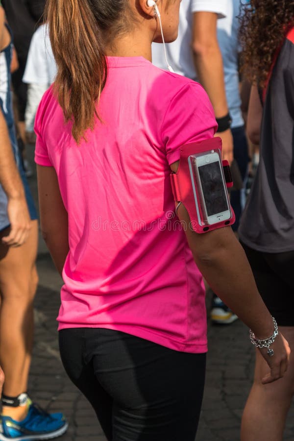La fille avec le T-shirt rose et le brassard de Smartphone enferment l'attente au RU photo stock La fille avec le T-shirt rose et le brassard de Smartphone enferment l'attente au RU photo stock