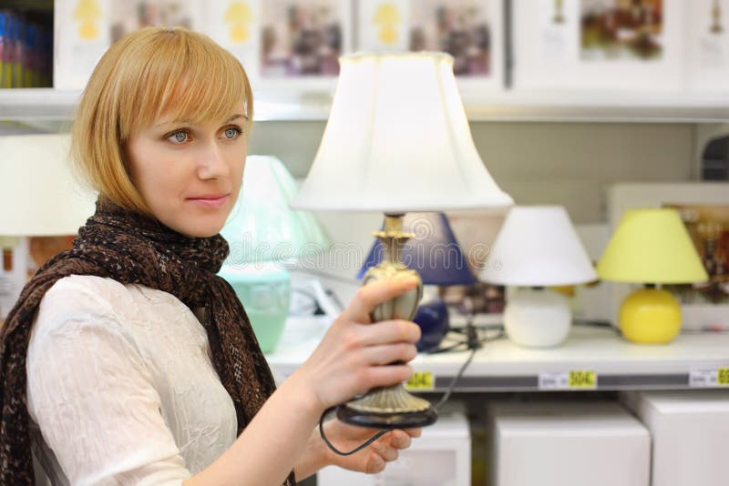 La fille blonde retient la belle lampe de table dans le système photo stock La fille blonde retient la belle lampe de table dans le système photo stock